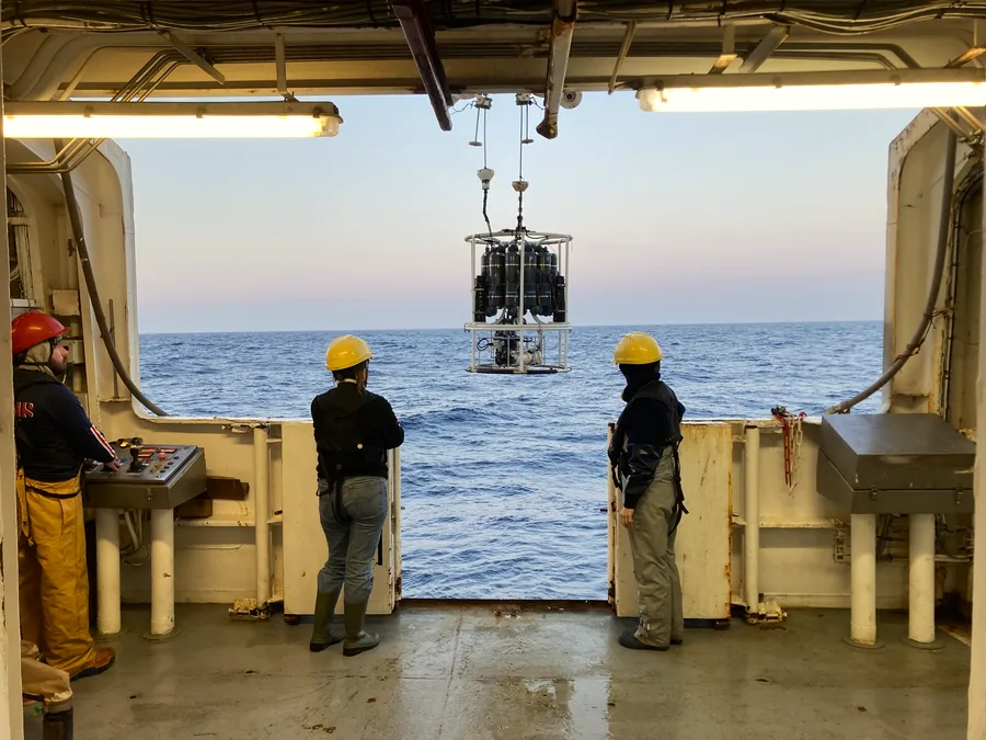 A CTD probe and rosette of Niskin bottles being launched from a research vessel