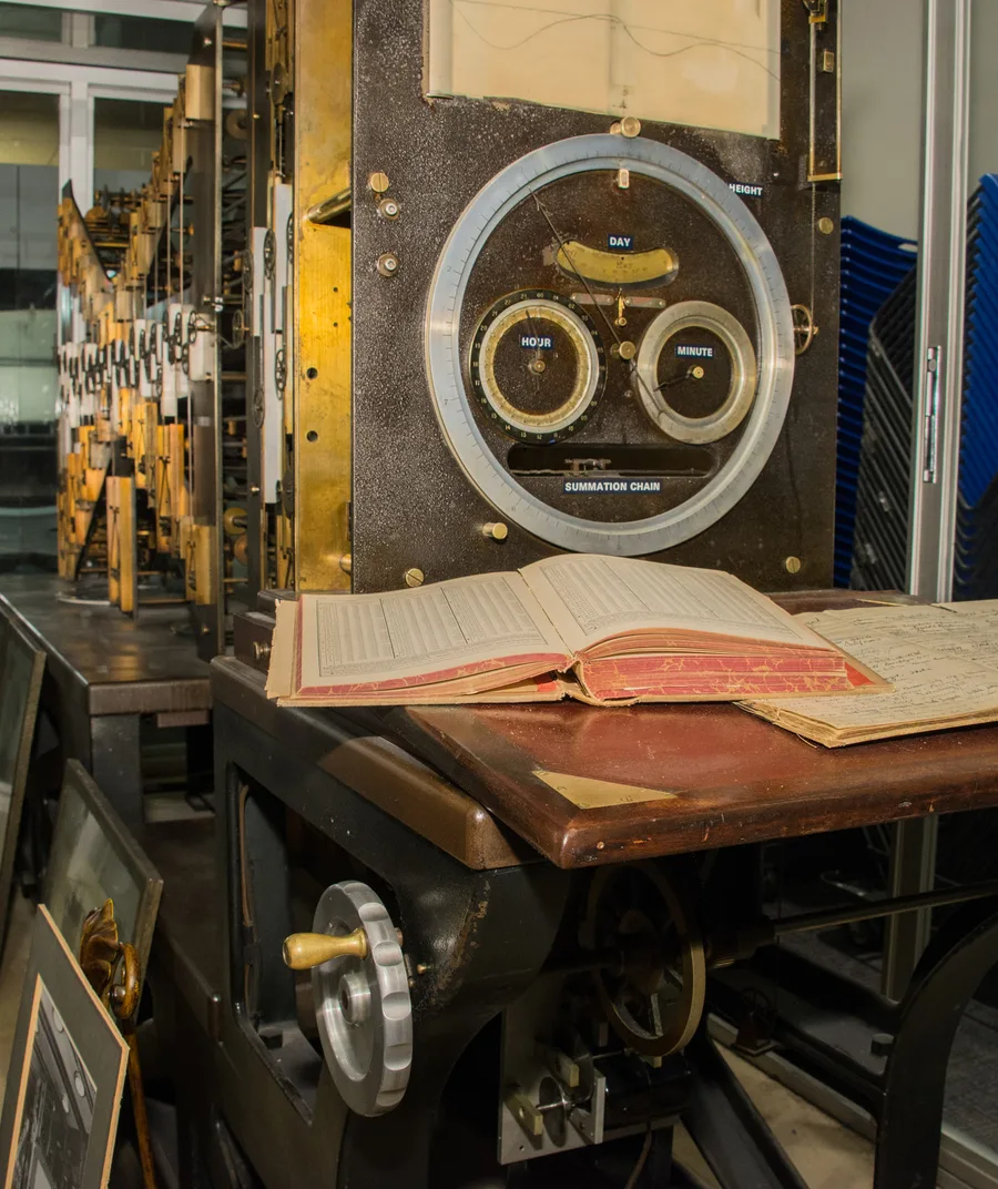 Detail of Tide Predicting Machine No. 2, nicknamed Old Brass Brains, showing its day/hour/minute dials and an open logbook
