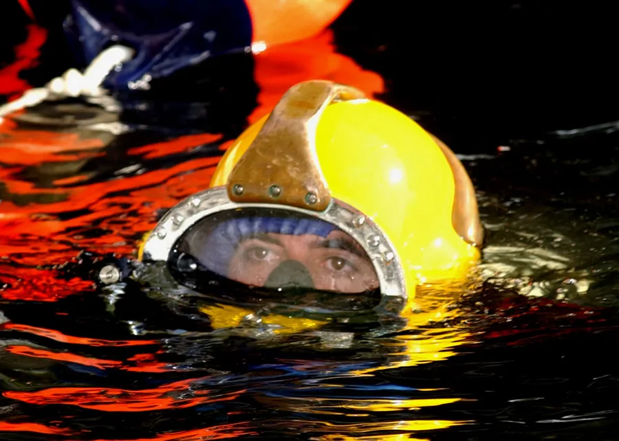 A Navy diver in an MK-21 deep sea diving helmet preparing to descend for underwater construction work