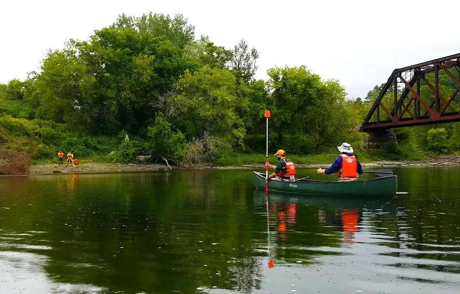 A USGS employee taking channel measurements from a canoe using a survey prism and total station