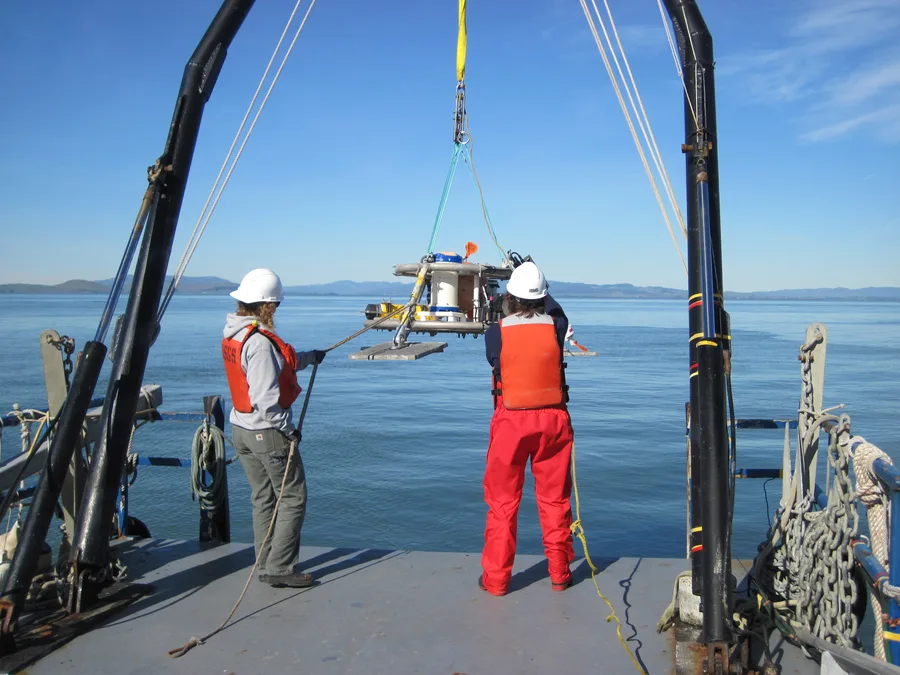 Two researchers deploying an ADCP instrument frame from the deck of a survey vessel