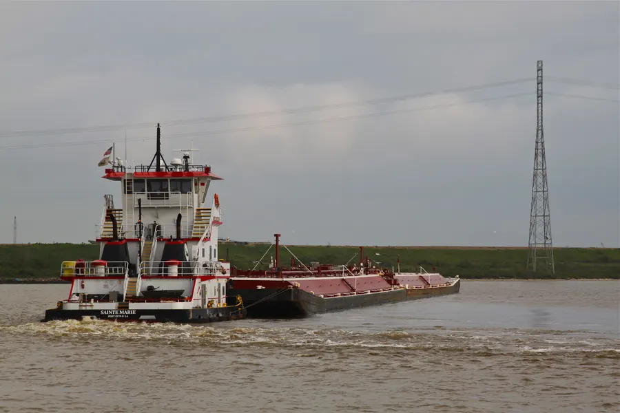 Tugboat guiding a barge through the Houston Ship Channel, a narrow channel with dense vessel traffic