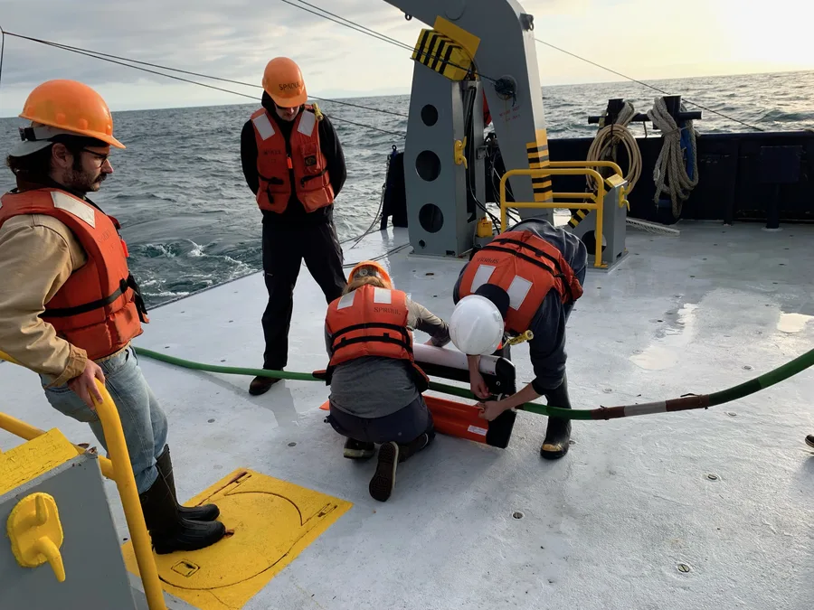 Researchers on the deck of a vessel deploying a seismic streamer with a depth-control bird attached