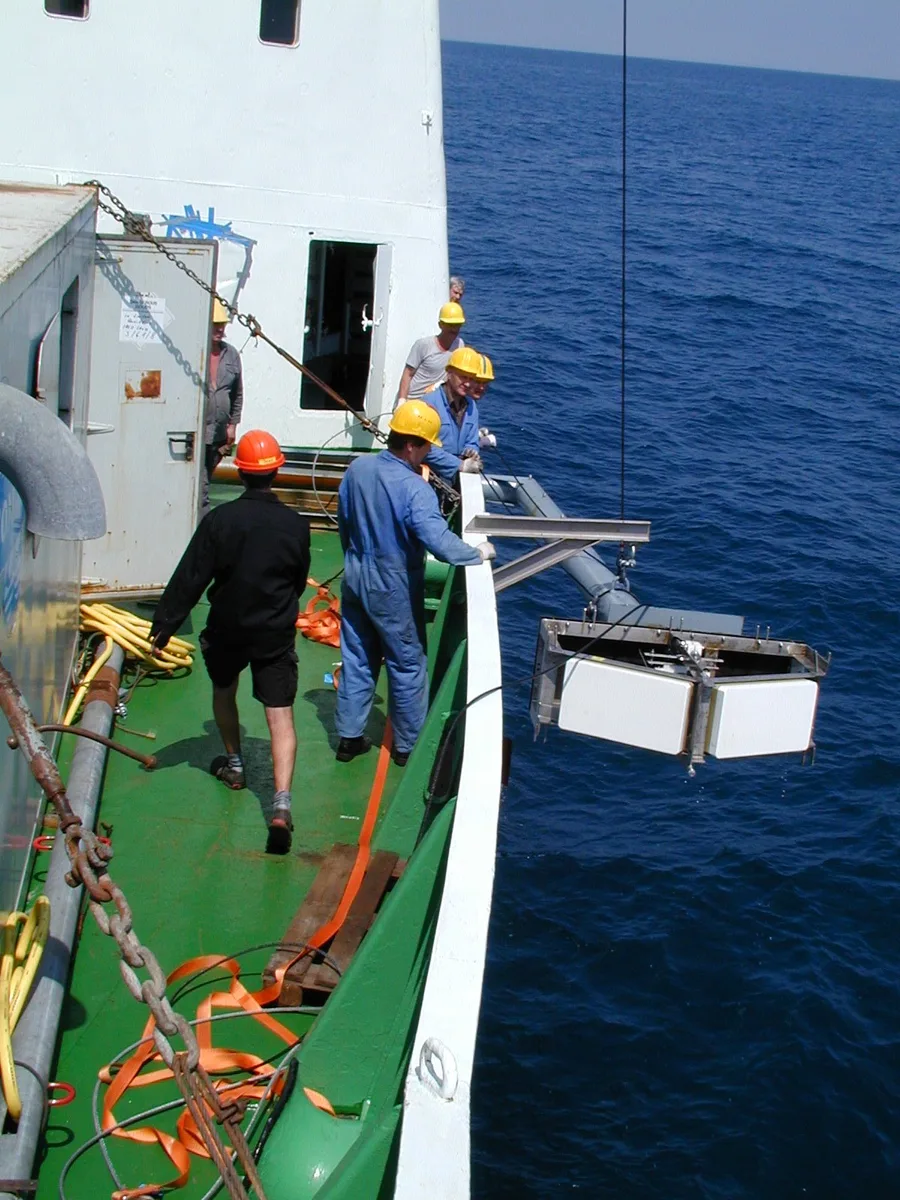 Crew deploying a multibeam echosounder transducer from the side of a research vessel